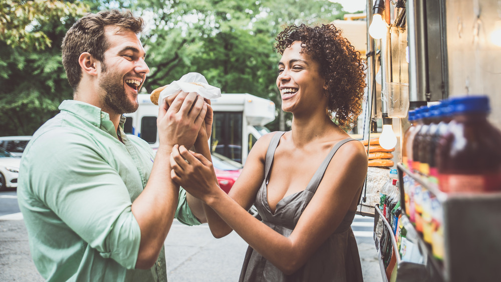 Millennial couple eating hot dogs from food cart