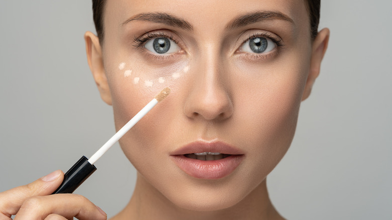 Woman applying concealer to under eyes