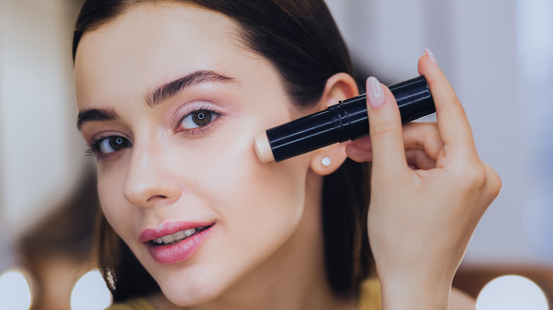 A woman using a concealer stick on her face.