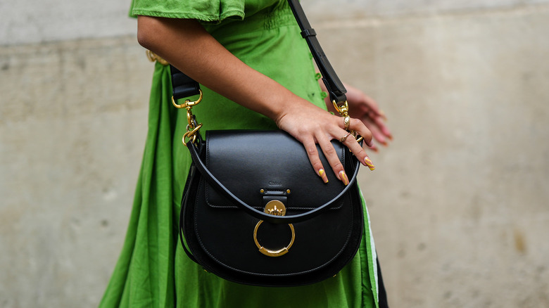 Model in green dress carrying a black crossbody bag
