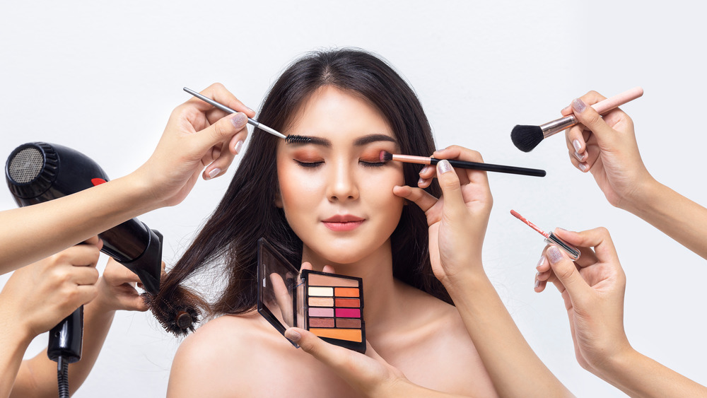 Multiple hands doing makeup, hair on woman