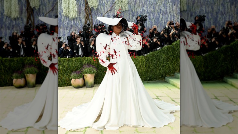 Naomi Osaka in a billowing white dress with a matching hat and red leaves sprouting out of it at the 2026 MET Gala