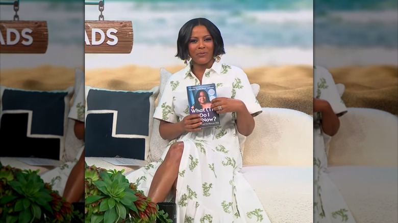 Tamron Hall holding a book in a white dress.