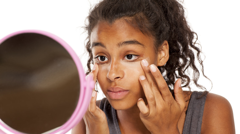 Woman applying concealer in front of pink mirror