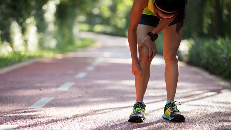 Female runner bending over with knee pain on trail