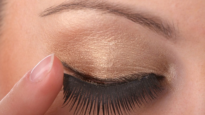 Young woman applying false eyelashes with her finger