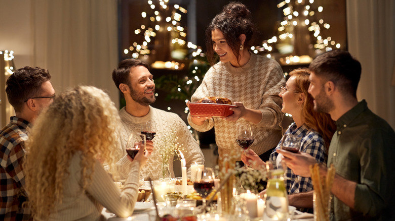 Woman serving a dish with all of her friends sitting around a holiday table