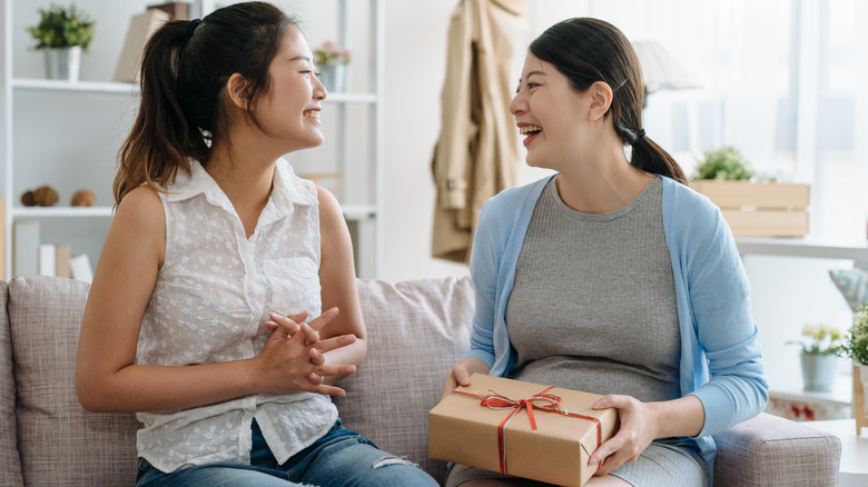 person giving another one a gift, while sitting on the couch