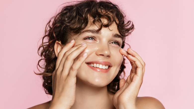 Woman applying skincare to cheeks while smiling 