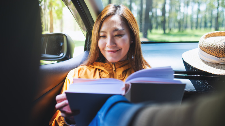 Happy Asian woman reading while riding in car
