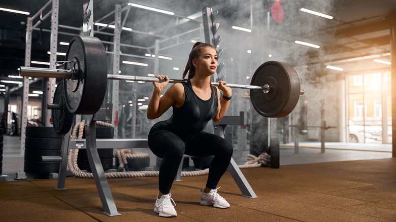 powerlifter squatting in fitness studio gym and using heavy barbell for a squat