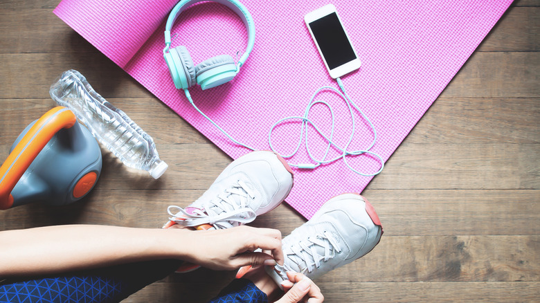 Woman wearing tennis shoes and workout leggings with her stuff laying on a pink yoga mat.