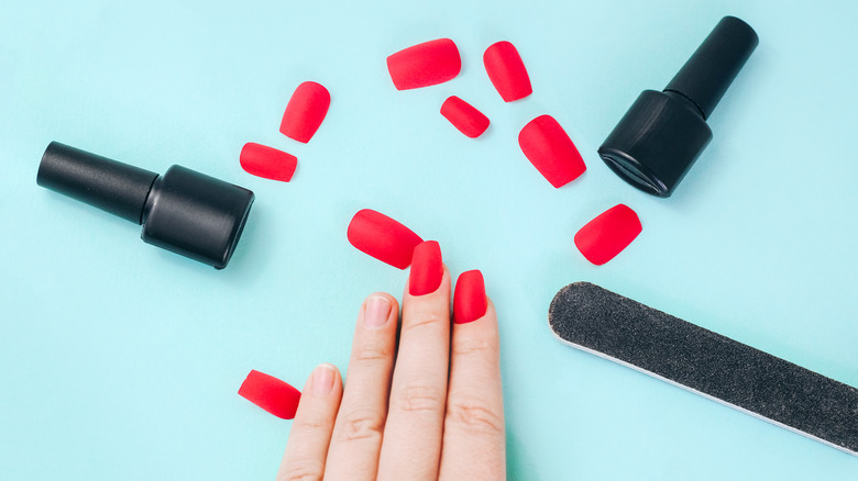Bright red press on nails, a nail file and nail polish bottles