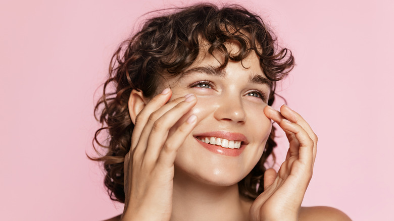 Woman applying skincare to cheeks while smiling 