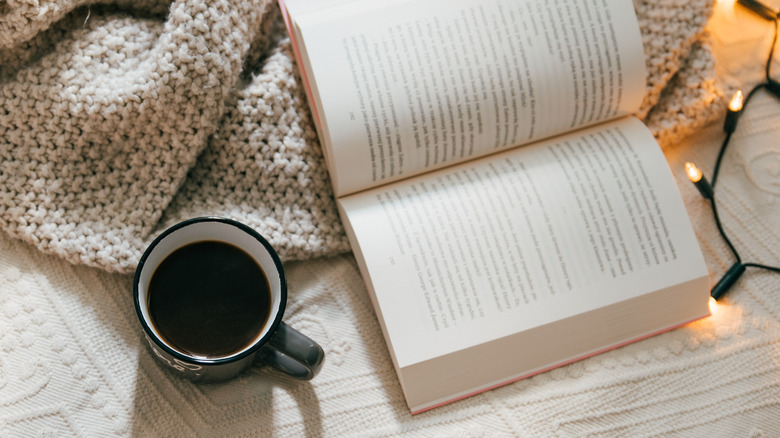 top view of a clozy blanket, open book, and mug of tea