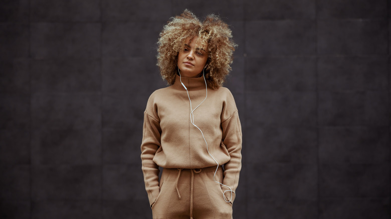 girl in tracksuit standing with hands in her pockets and listening music