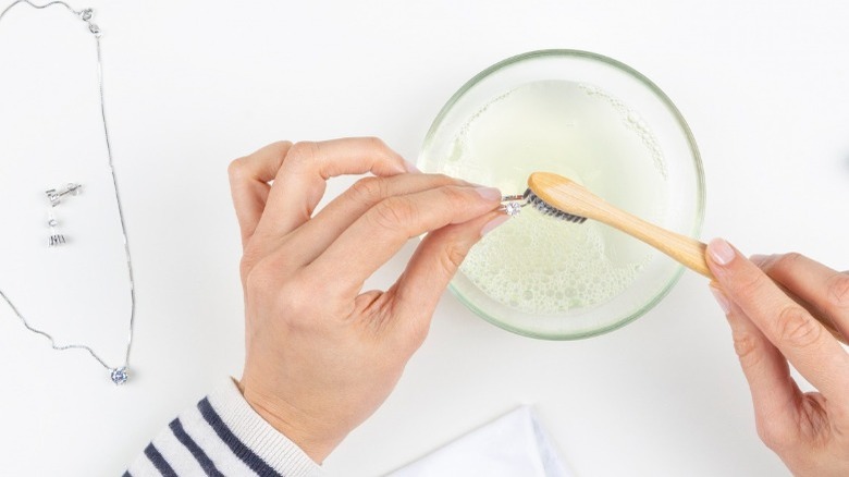 Woman cleans silver ring with soapy water and natural-fiber brush