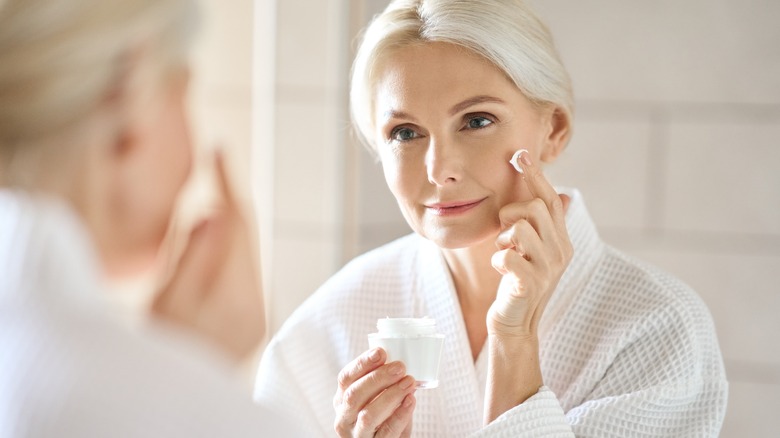 An older woman applying cream in the mirror