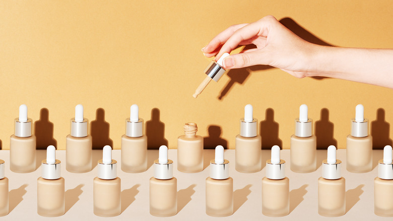 Woman holding a foundation dropper above many bottles of foundation