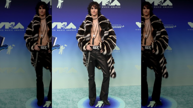 Sombr posing in a fur coat, leather pants, and no shirt
