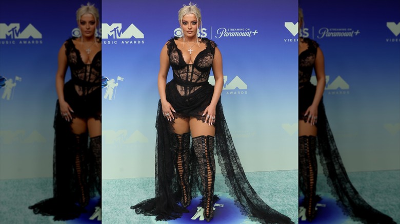 Bebe Rexha posing in a black lingerie-inspired dress with thigh-high boots