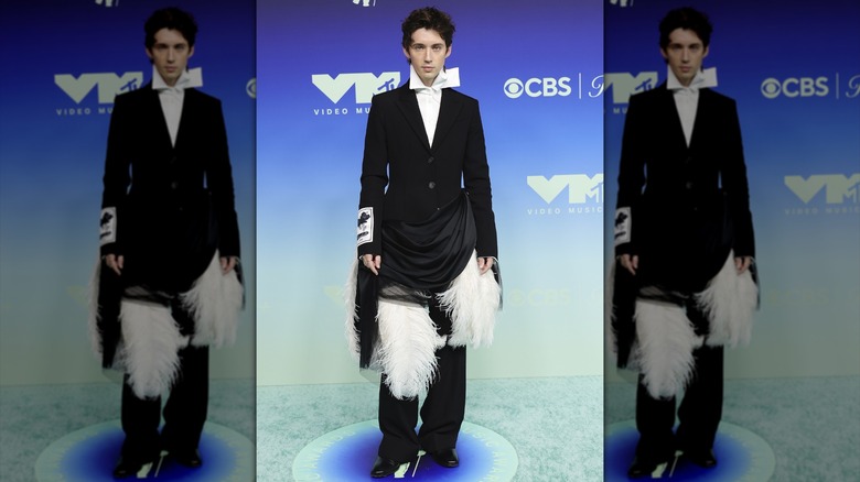 Troye Sivan posing in a suit with big, white feathers around the hips