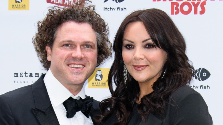 Martine McCutcheon and Jack McManus in black formals smiling on step-and-repeat