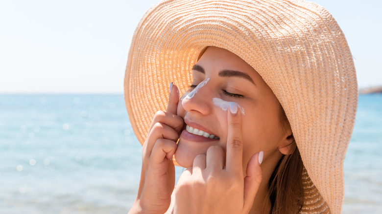 woman at beach applying sunscreen wearing hat