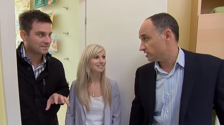 David Visentin from Love It or List It looks concerned talking to a smiling couple in a yellow room of a new house.