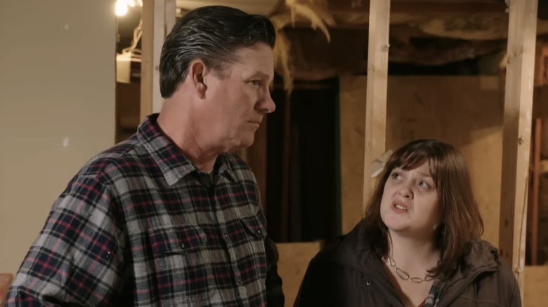 On Love It or List It upset homeowners stand in an unfinished basement with the woman looking up at her husband.