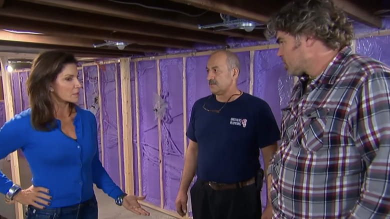 Love It or List It's Hilary Farr stands in an unfinished basement looking concerned talking to two contractors.
