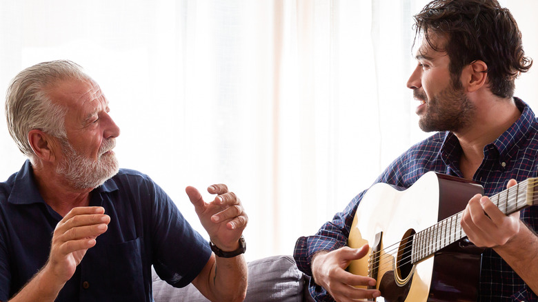 Annoyed senior father with his grown son playing guitar on the couch 