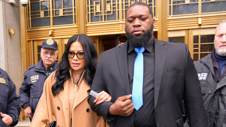 Jen Shah in sunglasses and camel coat with unidentified escort leaving court