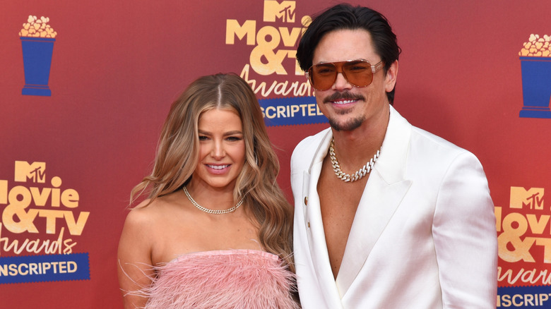 Tom Sandoval in cream blazer and sunglasses next to Ariana Madix in pink, feathered, strapless dress