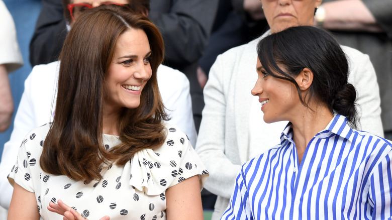 Kate Middleton and Meghan Markle looking at each other and smiling
