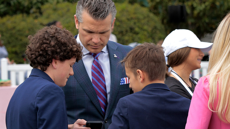 Pete Hegseth looking down at his phone at the White House Easter celebrations in 2025 while his two songs look over the screen.