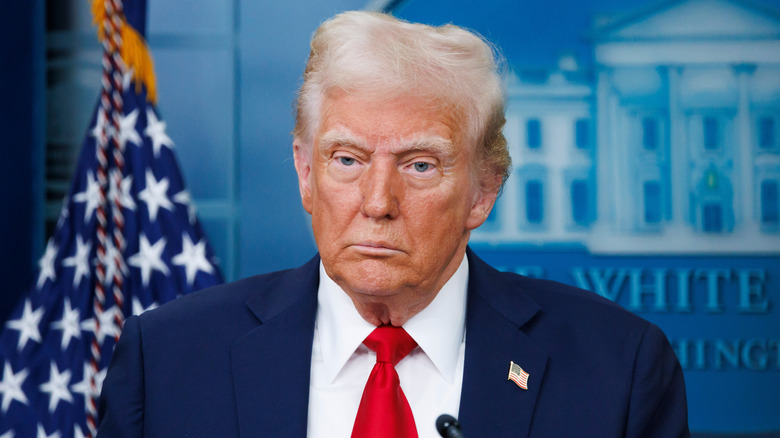 Closeup of Donald Trump standing in front of White House poster and American flag