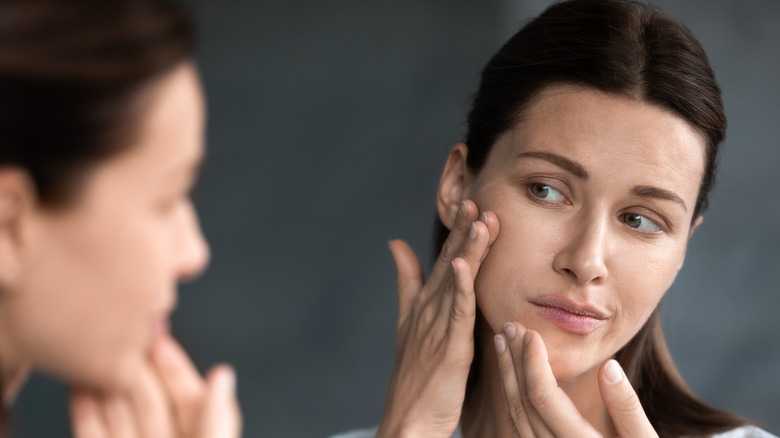 A woman inspecting her skin in a mirror