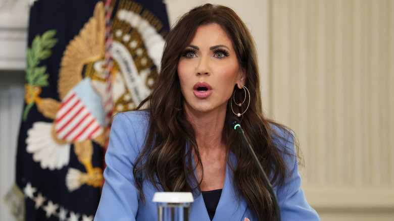 Kristi Noem looking shocked at an event in a light blue blazer