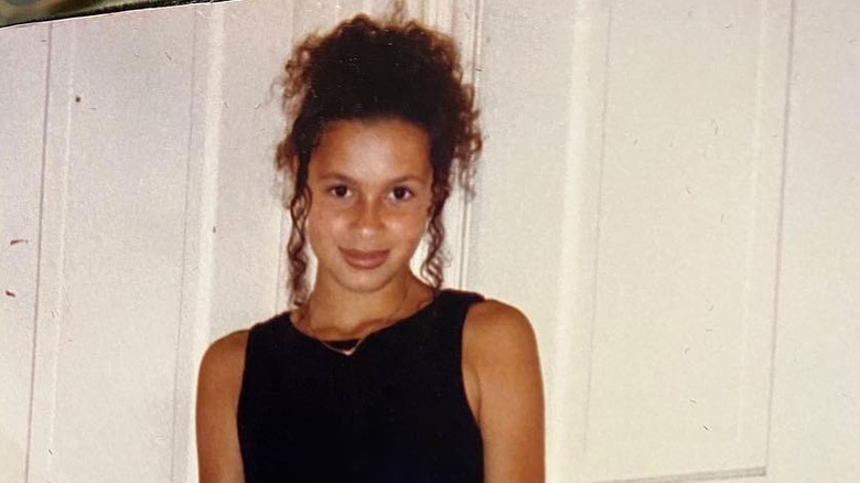 A young Joy Taylor poses against a white wall with her hair up.