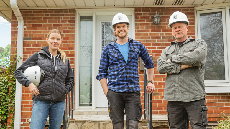 Sherry Holmes, Mike Holmes and Mike Holmes Jr. posing in front of a concrete background