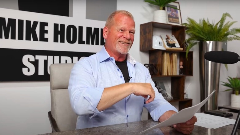 Mike Holmes sitting at a desk while recording an episode of his podcast