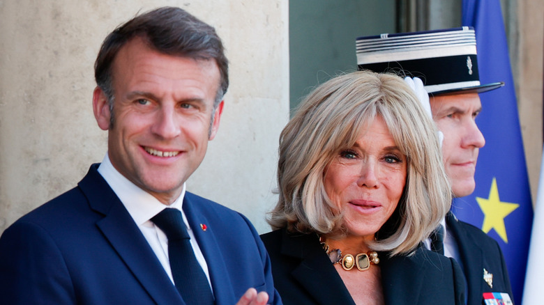 Emmanuel Macron with his hands folded standing next to Brigitte Macron