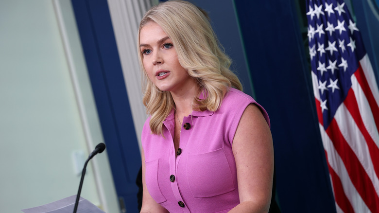Karoline Leavitt at podium in a pink dress with black buttons
