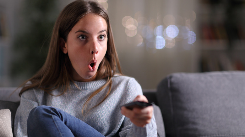 Woman with TV remote looking shocked