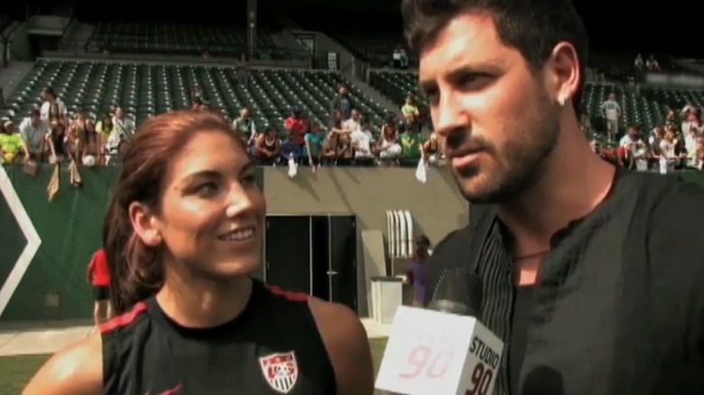 Hope Solo and Maksim Chmerkovskiy speaking with a reporter at a soccer match