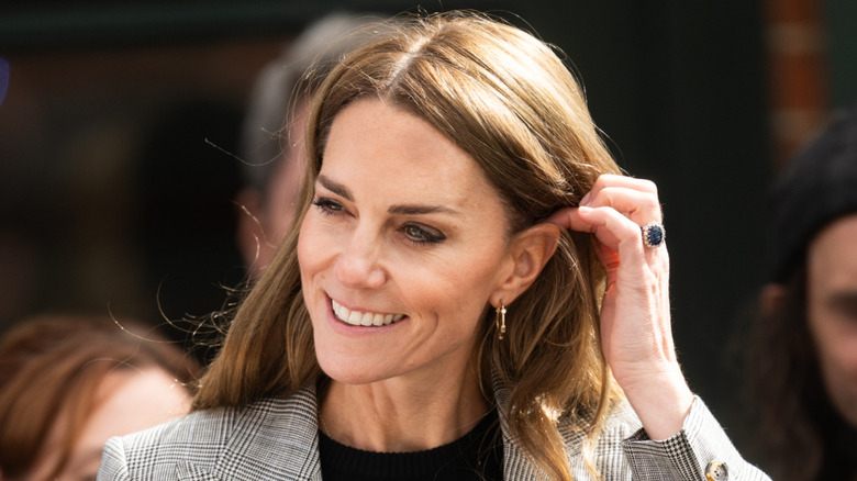 Kate Middleton smiling while tucking hair behind ear
