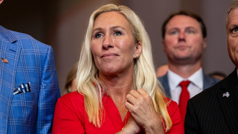Marjorie Taylor Greene clasping her hands together while wearing a red dress