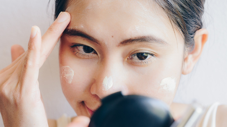 woman applying foundation in mirror