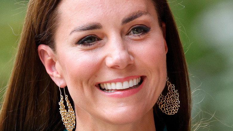 Kate Middleton smiling, wearing coral lipstick and earrings